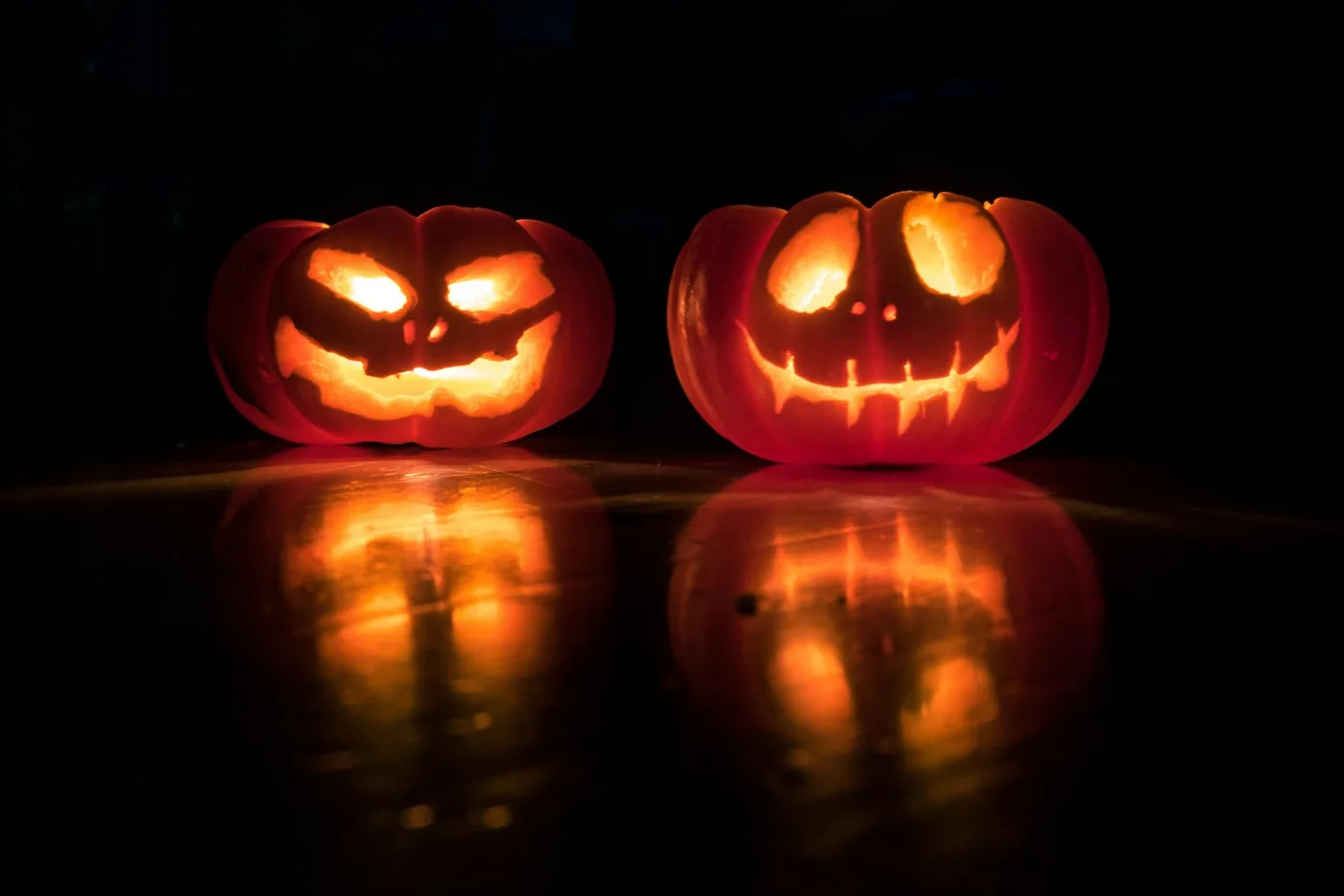 Two glowing carved jack-o’-lanterns against a dark background